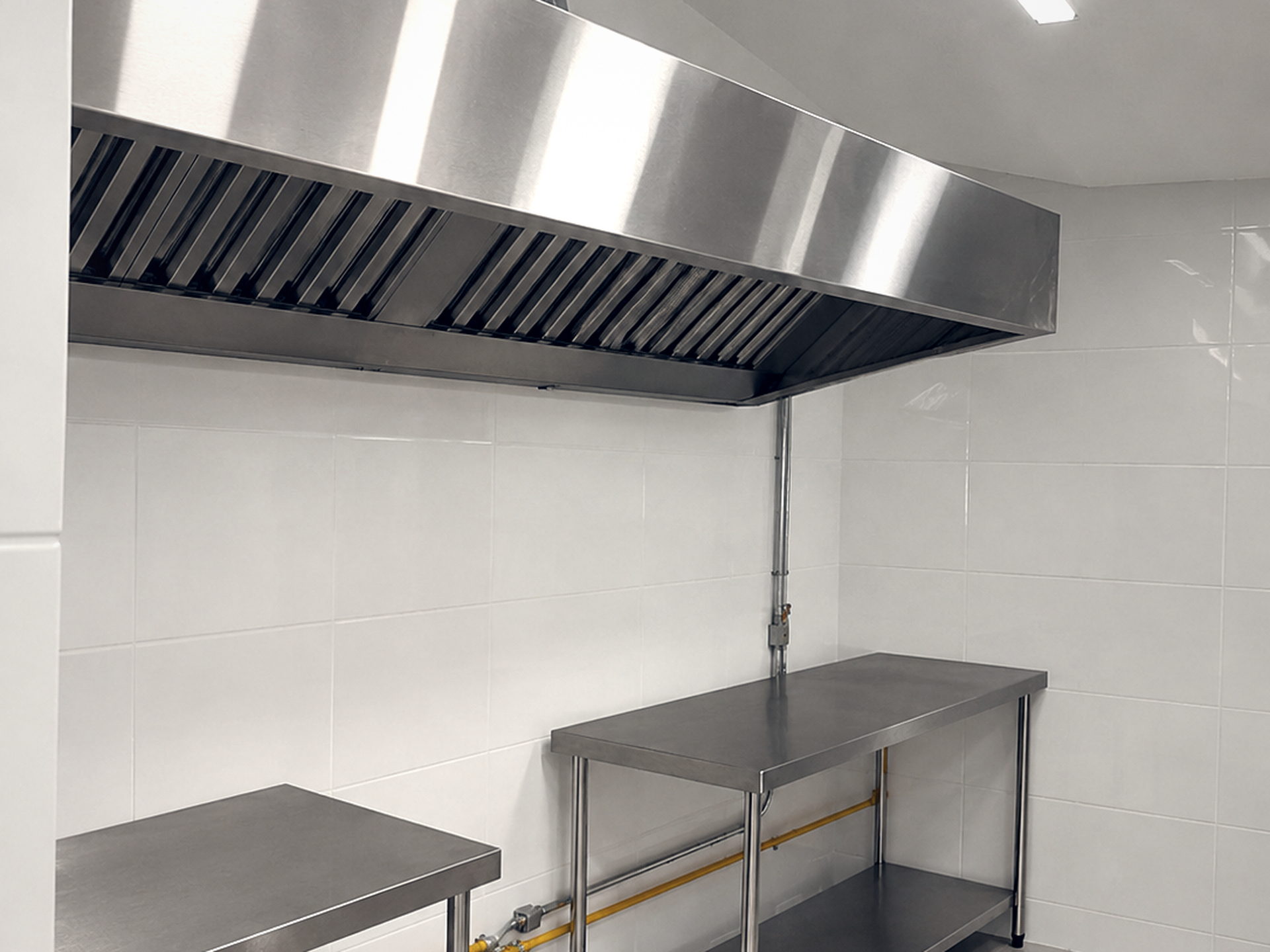 Coifa de parede em aço inox com bancadas de apoio em cozinha profissional